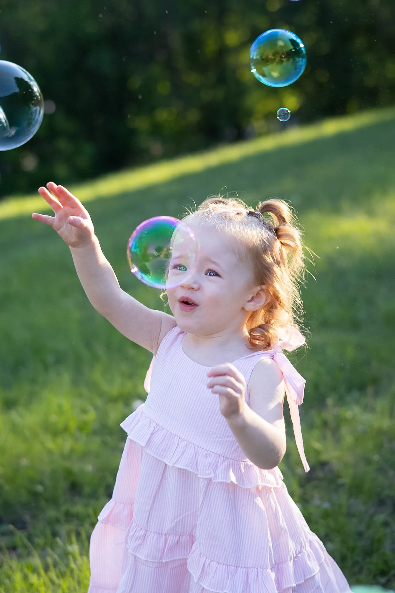 Young girl reaching toward bubbles in a sunny field.