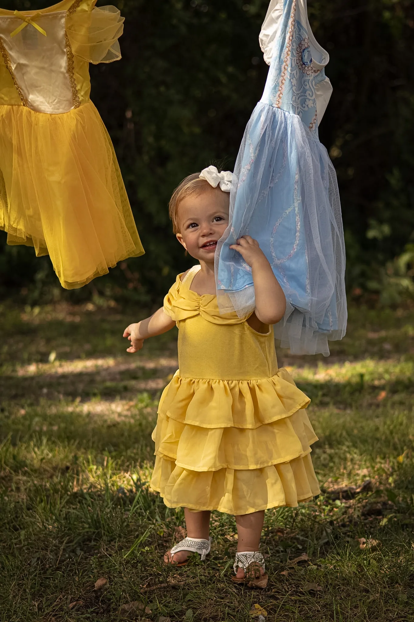 Young girl playing beside yellow dresses on a clothesline.
