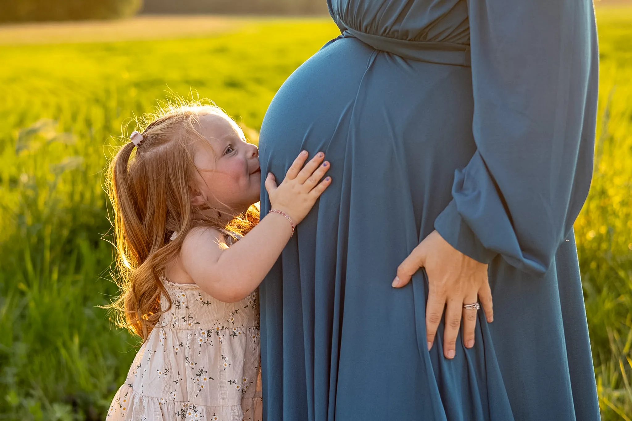 Young child gently kissing an expectant mother's belly.