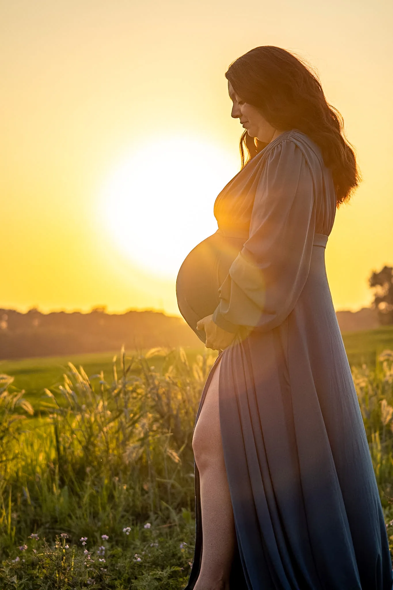 Expectant mother standing in a sunlit field.