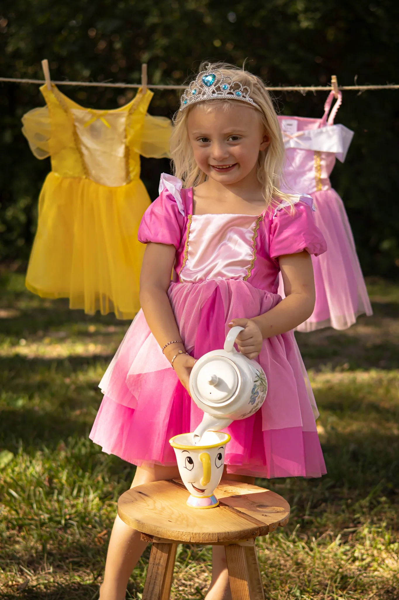 Young girl in a pink princess dress at an outdoor tea set.